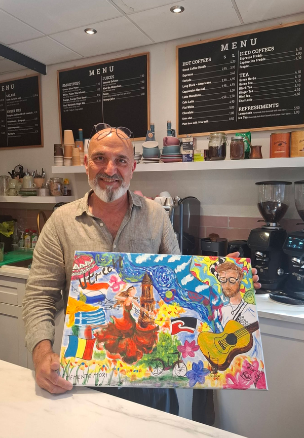 The coffee shop owner holding the finished painting we gave him, behind his counter