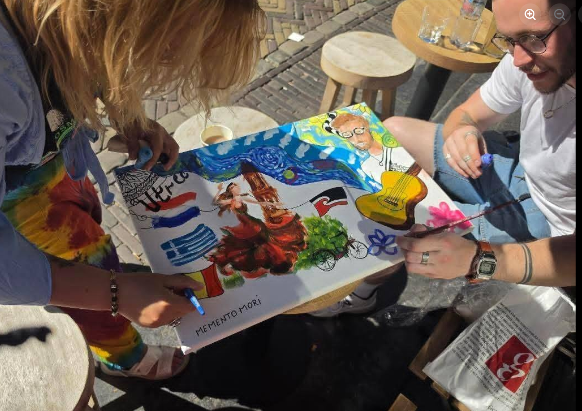 Close-up of hands adding paint to the shared canvas at an outdoor cafe table